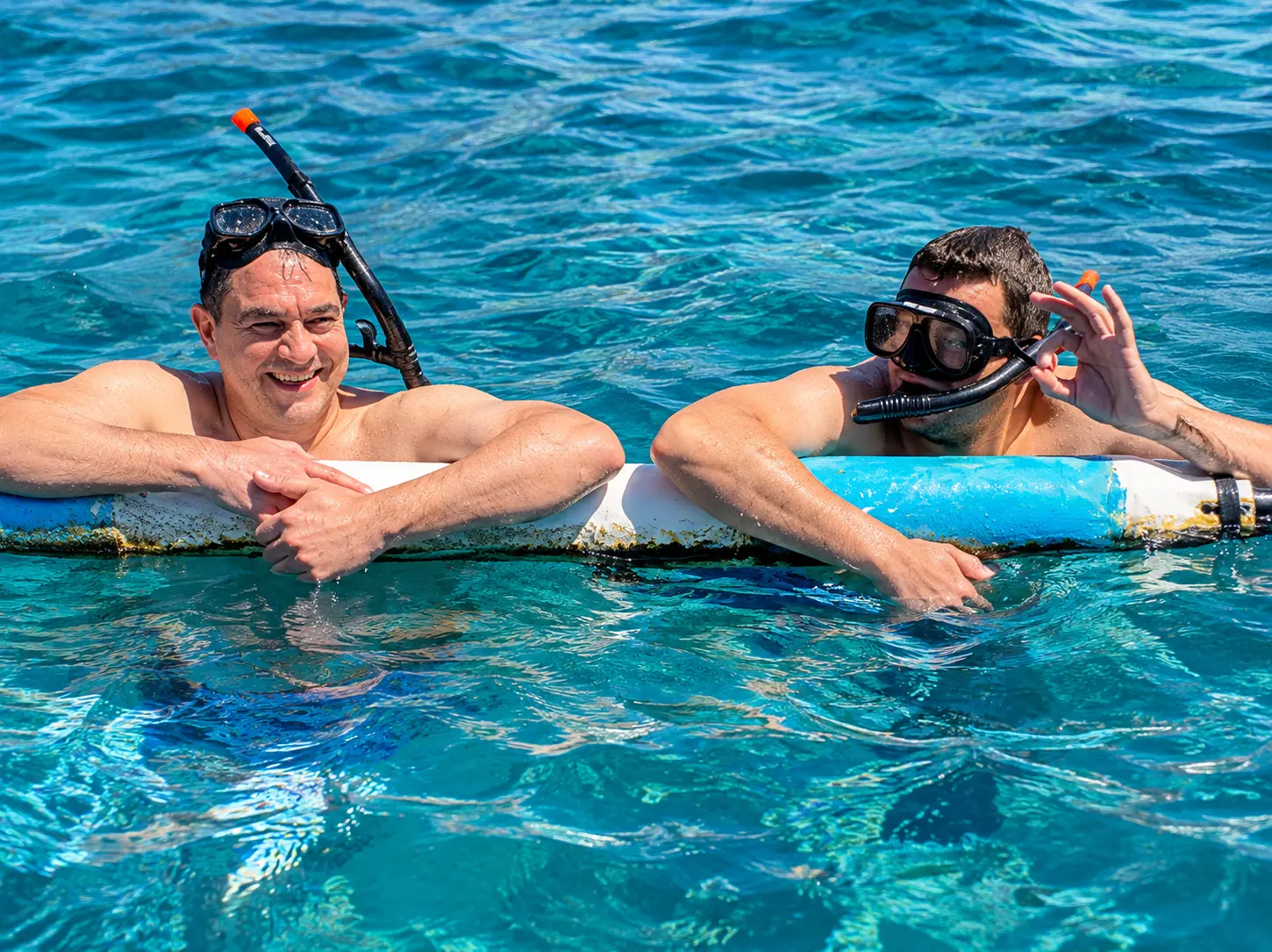 Two snorkelers resting on a floating buoy in the turquoise sea of Amed