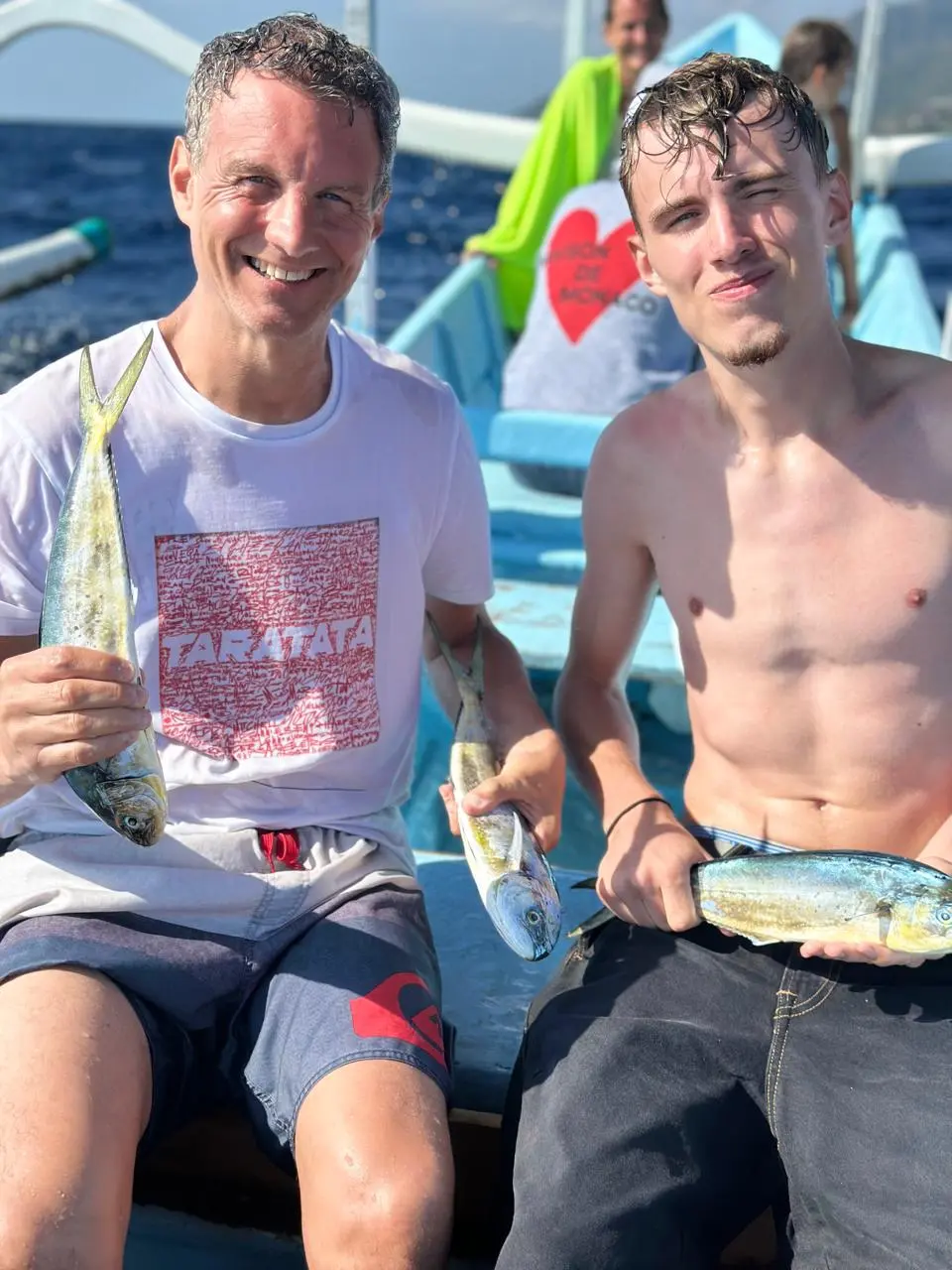 Father and son showing their catch aboard a traditional boat in Amed