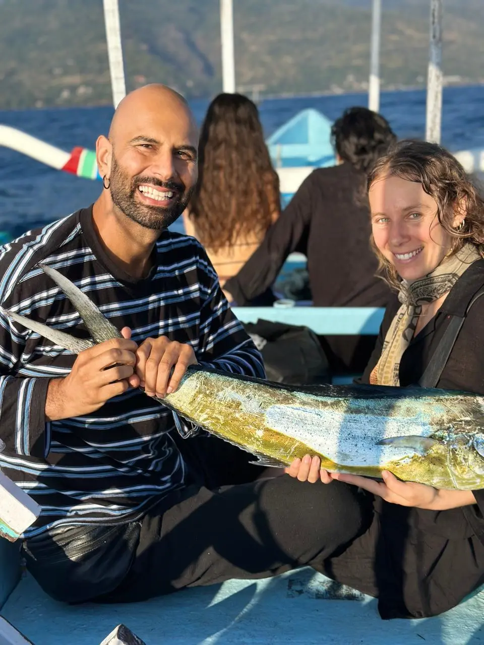 Couple holding a large mahi-mahi on a boat at golden hour in Amed