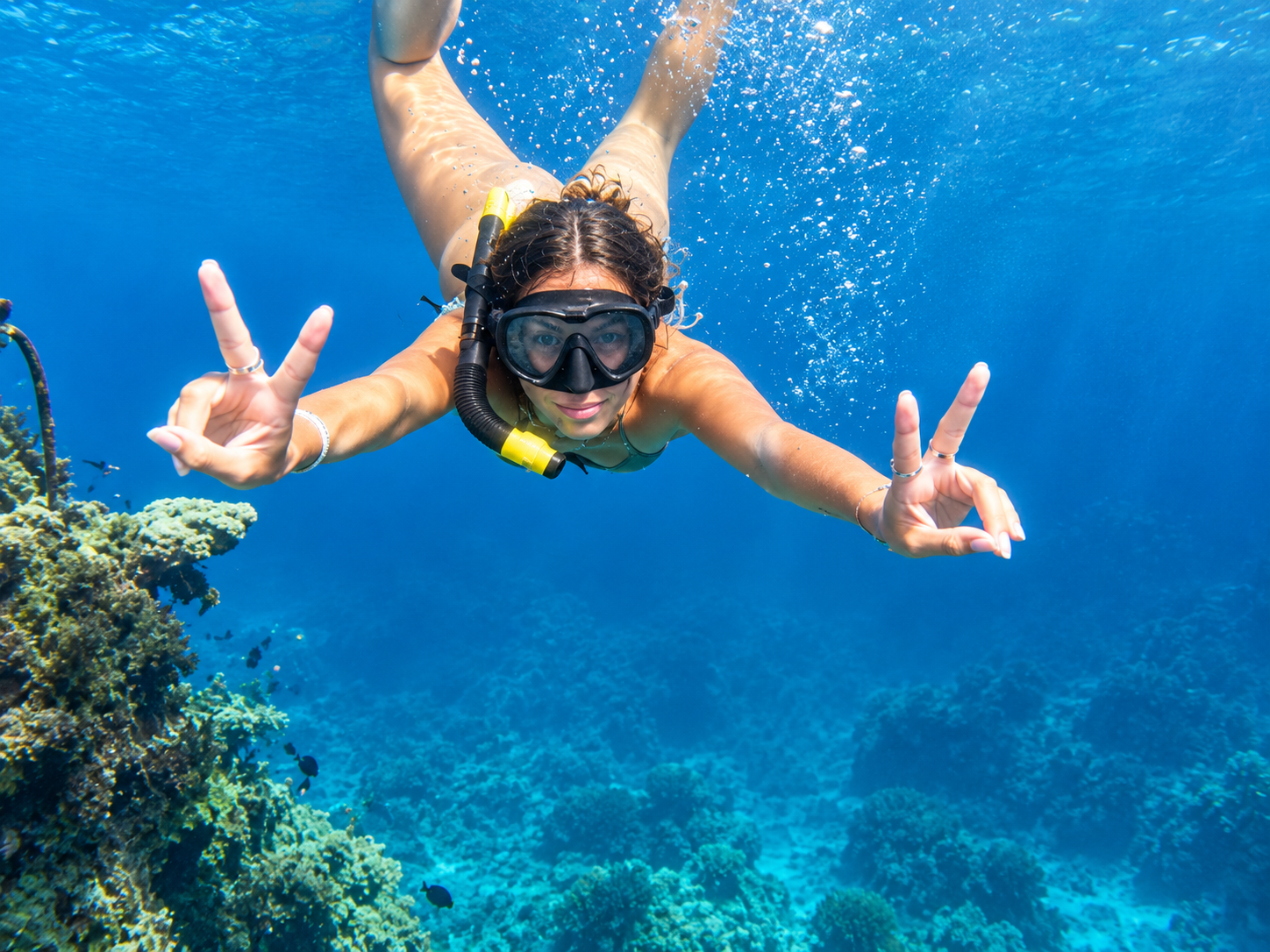 Snorkeler making a peace sign over a vibrant coral reef in Amed