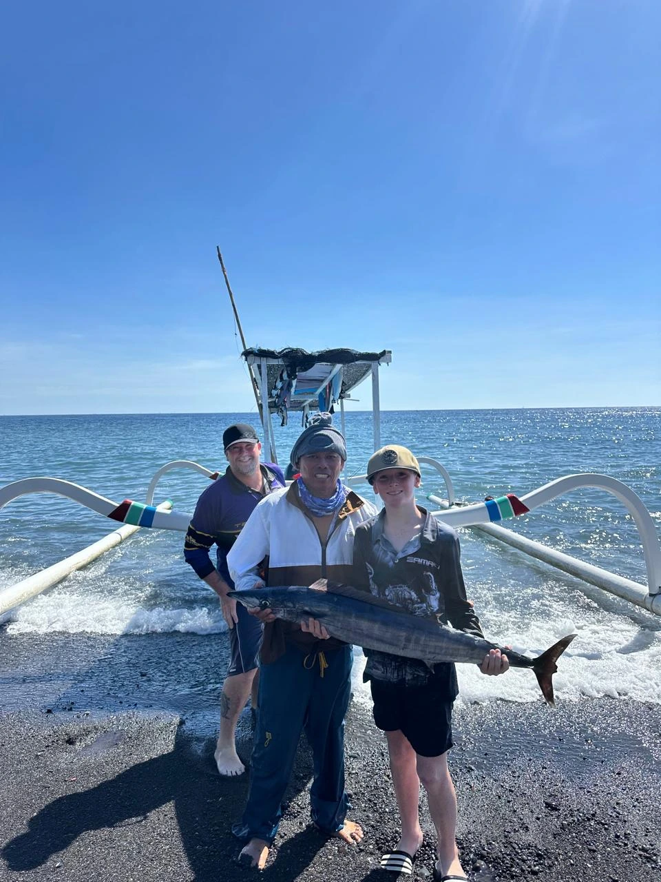 Anglers holding a freshly caught wahoo on Amed's black sand beach