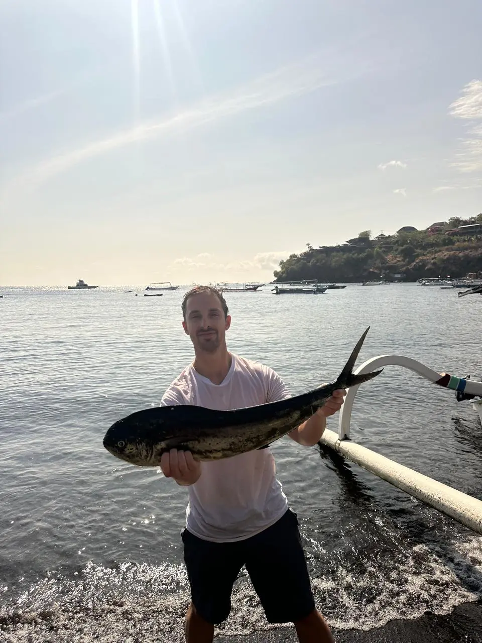 Angler proudly holding a large mahi-mahi on Amed's black sand beach